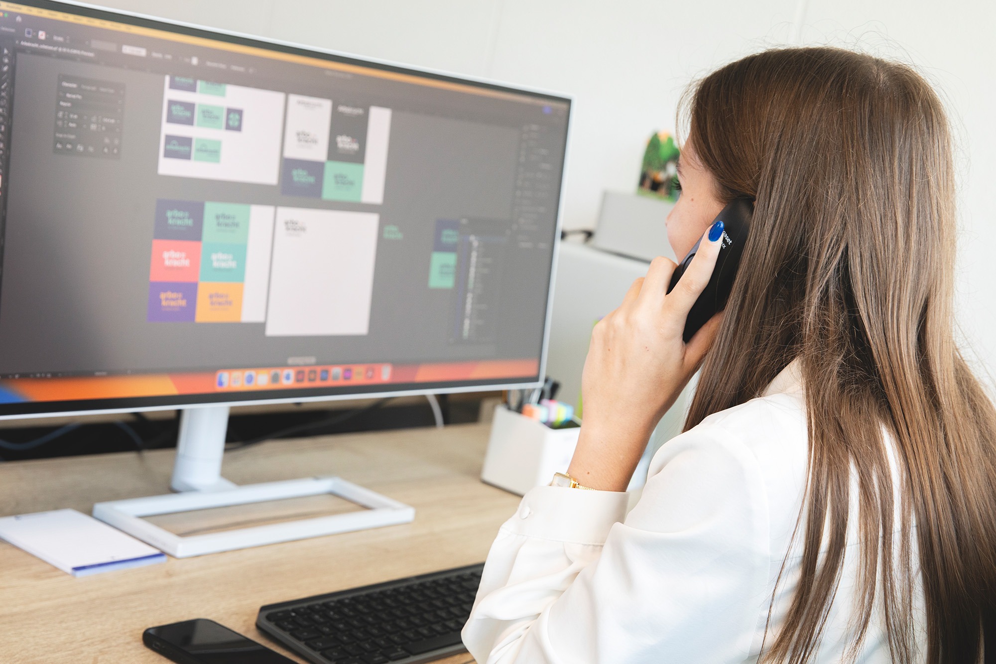 Medewerker van Marker Media ontwerpt visuele elementen op de computer en neemt telefonisch contact op met een klant.