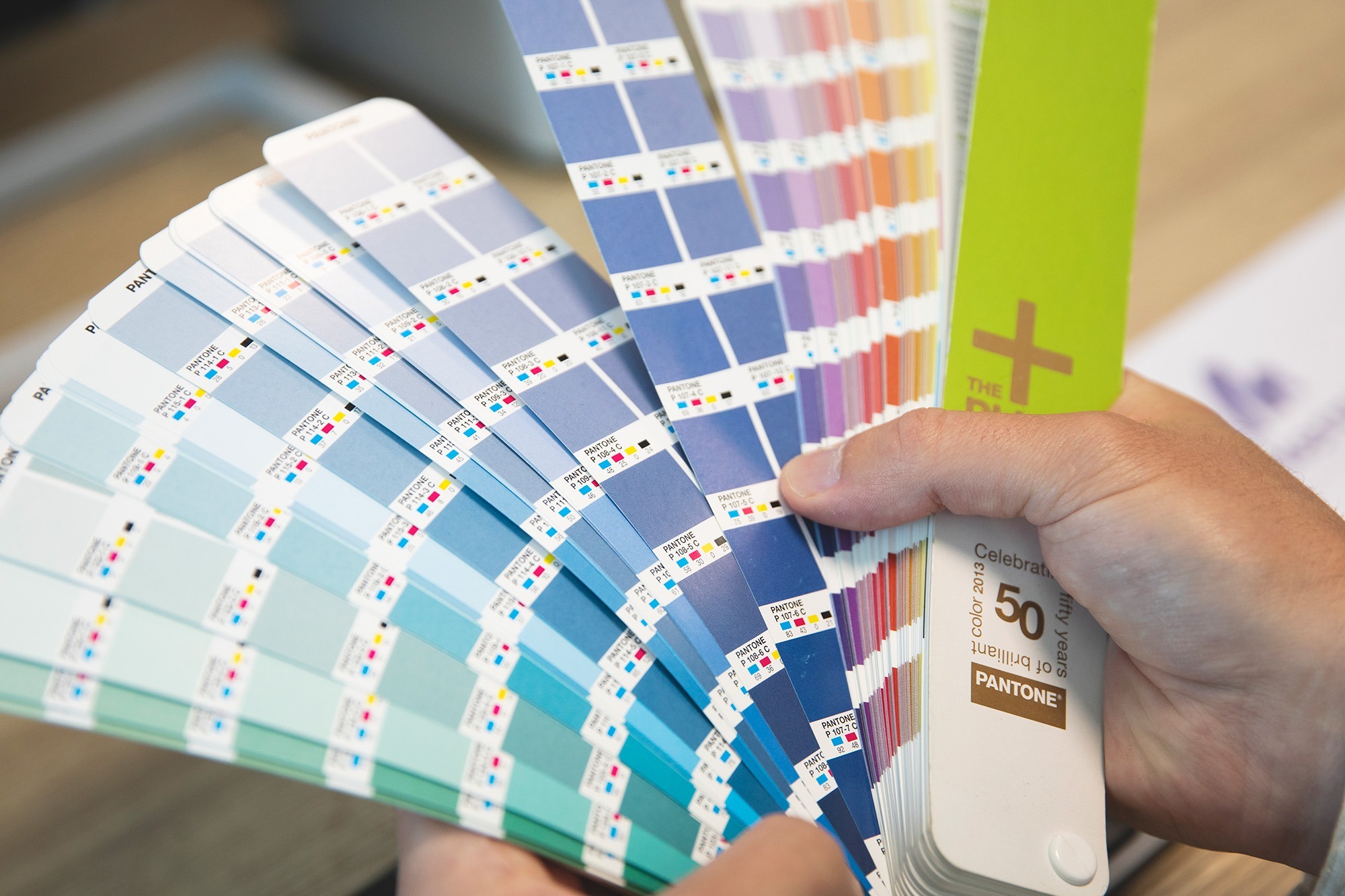 Medewerker van Marker Media bladert door een Pantone-kleurenwaaier voor nauwkeurige kleurkeuze bij ontwerpprojecten.