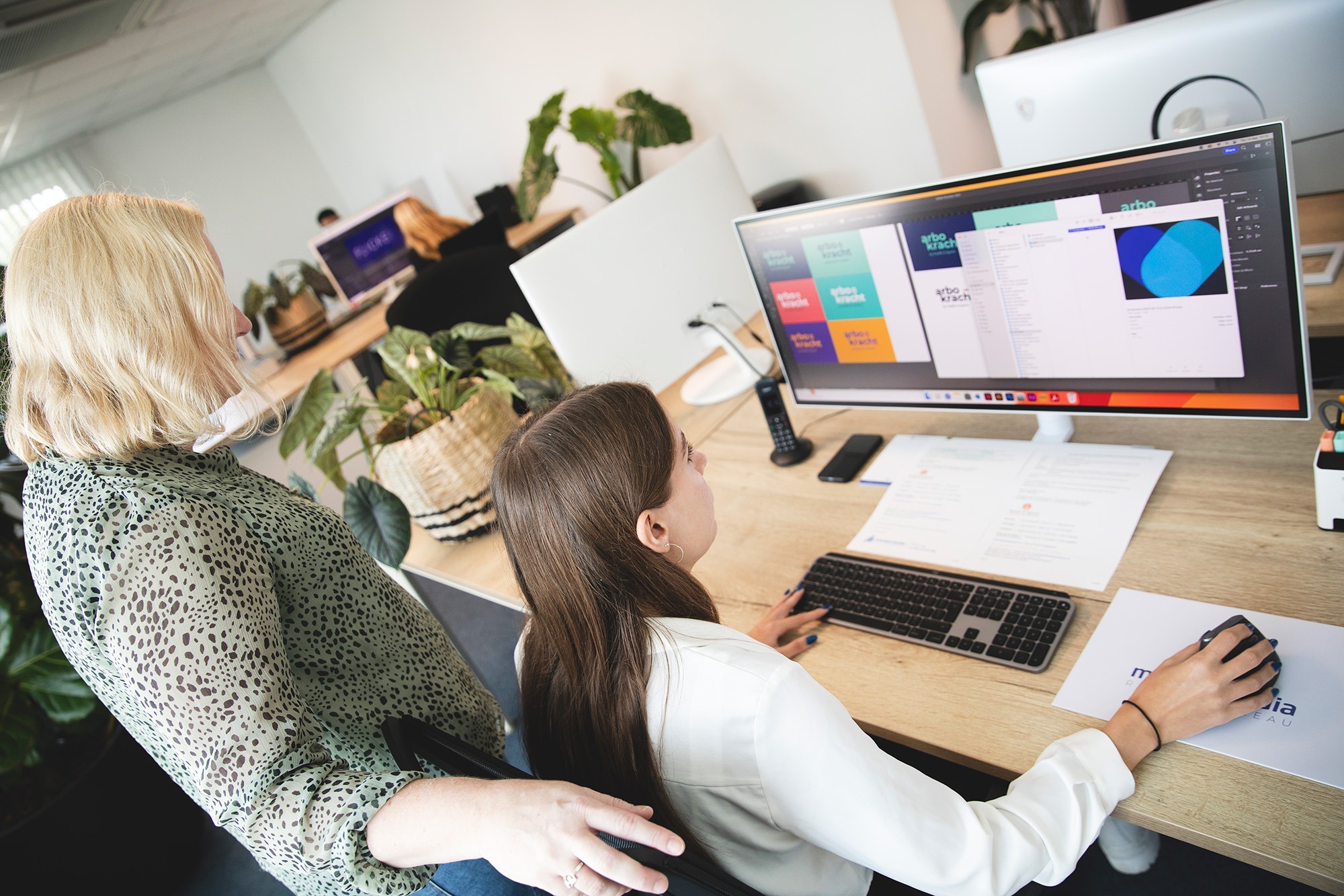 Medewerker van Marker Media ontvangt begeleiding tijdens het ontwerp van visuele branding op een groot scherm in een moderne kantooromgeving.