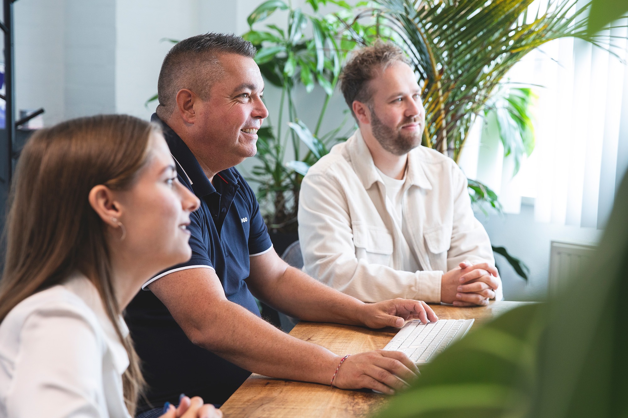 Teamleden van Marker Media werken samen tijdens een creatieve bespreking in een groene kantooromgeving. Chloé, Boyan en Marc die overleg plegen, over ons