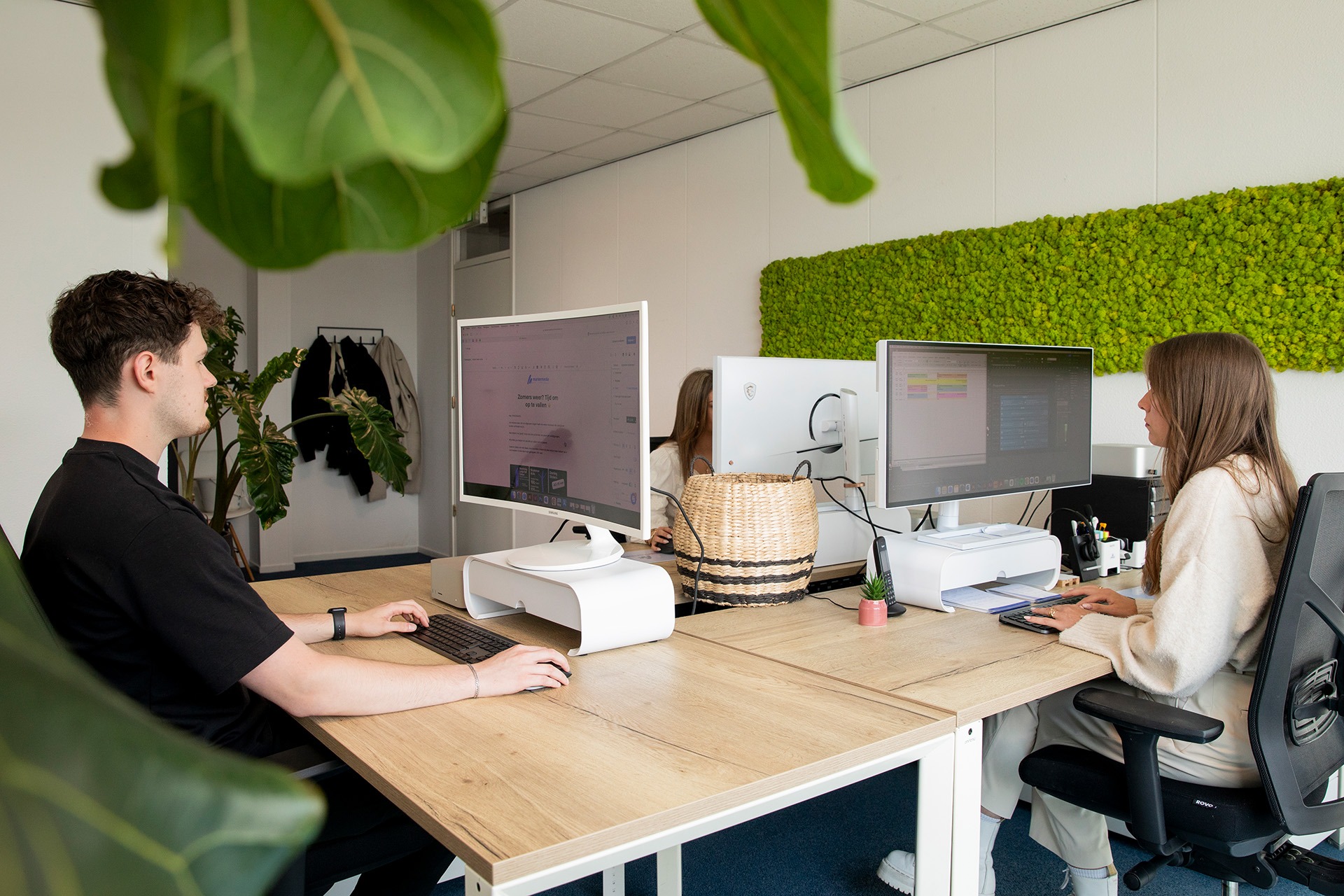 2 mensen achter beide hun eigen computer. Op een beeldscherm is het emailmarketing programma mailblue te zien en op het andere de planning in de agenda app van outlook